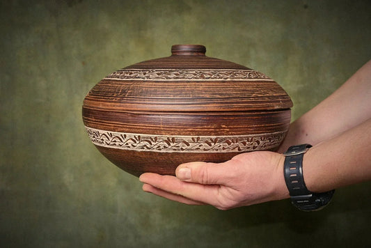 Handmade brown clay pot with a matching lid featuring intricate white carved patterns