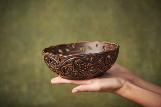 Handmade brown clay bowl with intricate carved patterns held in two hands