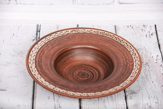 Handmade clay pasta bowl with decorative rim on rustic white wooden table