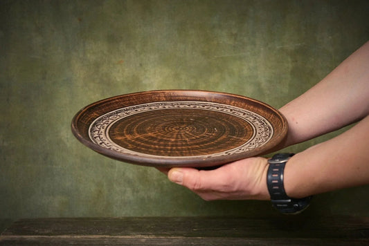 Hand holding a handmade brown clay plate with intricate circular carved patterns