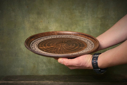 Hand holding a large handmade ceramic pizza plate with clay pattern, artisan kitchenware