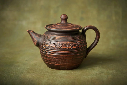 Handcrafted clay teapot with engraved design, artisan pottery home décor on green background