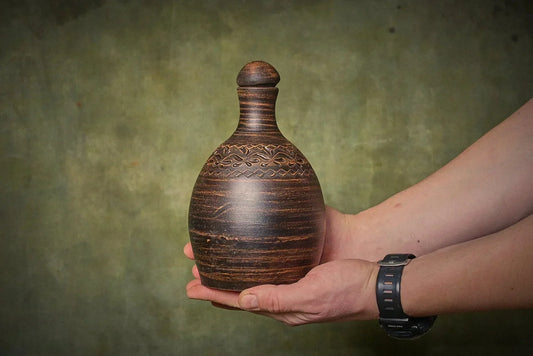 Hand holding a handmade engraved clay water bottle ceramic amphora by clayproductsshop