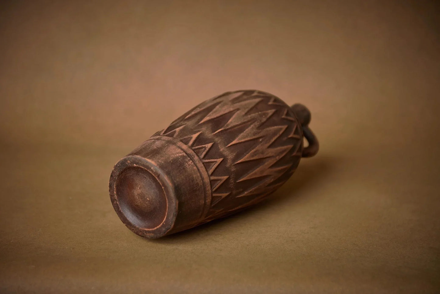 Handmade brown clay vase with geometric carved patterns resting on its side