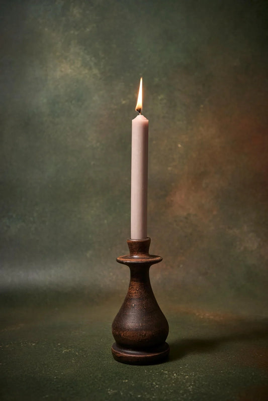 Handmade dark clay candle holder with a lit white taper candle against a moody green backdrop.