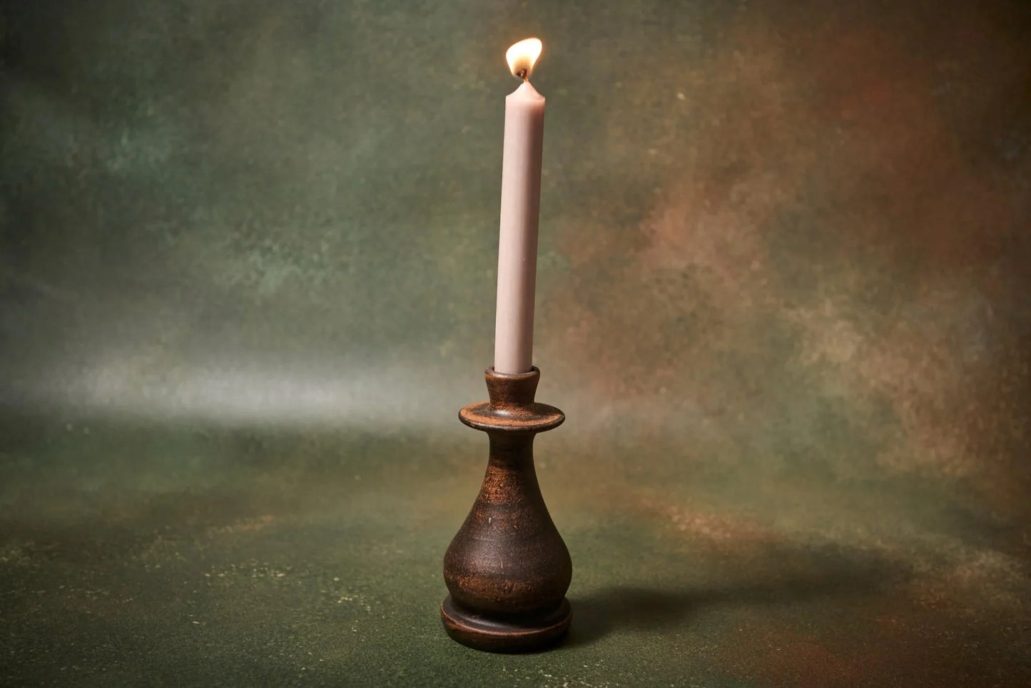 Handmade dark clay candle holder with a lit white taper candle on a textured background.