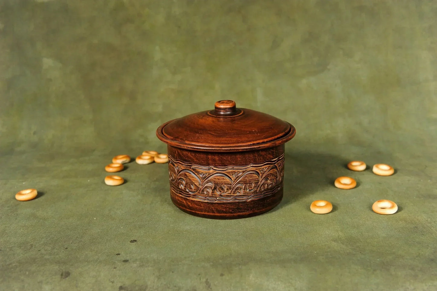 Handcrafted wooden storage box with intricate carvings, surrounded by small wooden rings on a green backdrop.