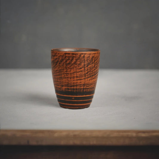 Handmade terracotta clay cup with dark textured patterns and horizontal stripes.