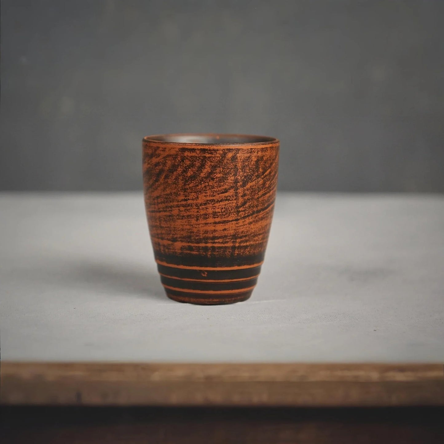Handmade terracotta clay cup with textured dark brown patterns and striped base.