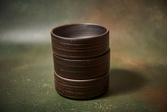 Stack of three handmade dark brown clay bowls on a textured green surface