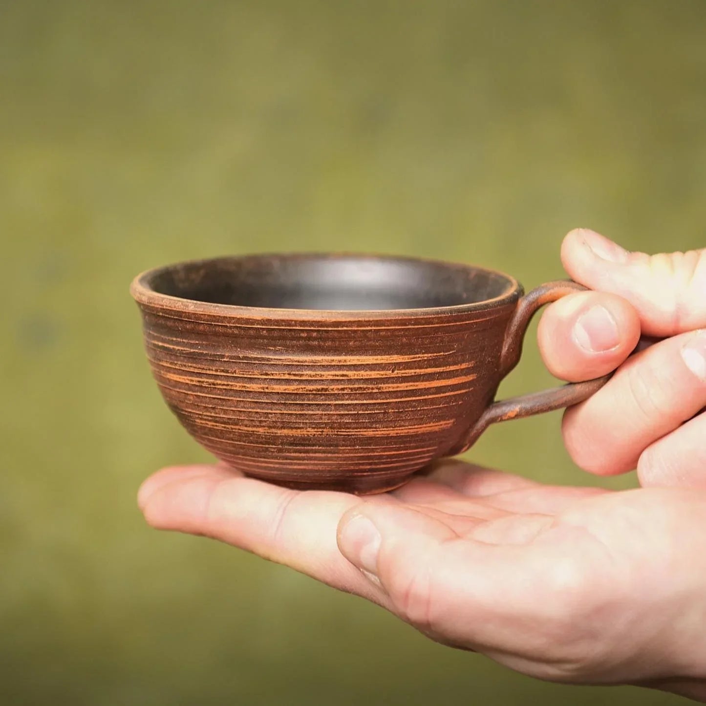 Hand holding a rustic handmade brown clay tea cup with horizontal texture