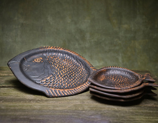 Handmade dark clay fish-shaped serving plates on a rustic wooden surface.