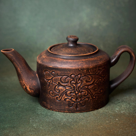Handmade clay teapot with intricate floral carvings, artisan-crafted for rustic home décor