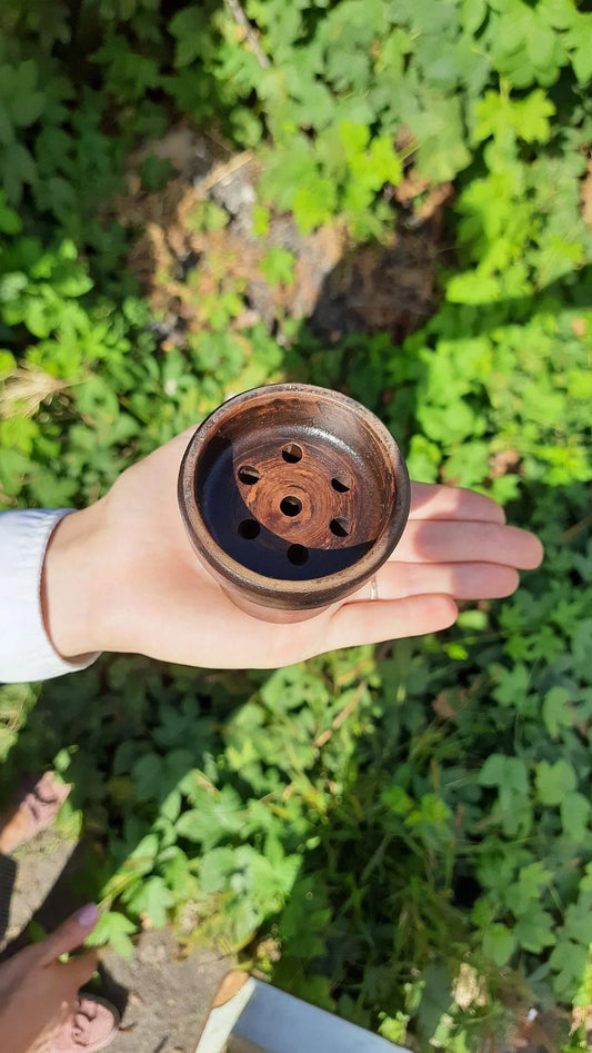 Handmade dark clay incense burner held in hand against a lush green garden background.