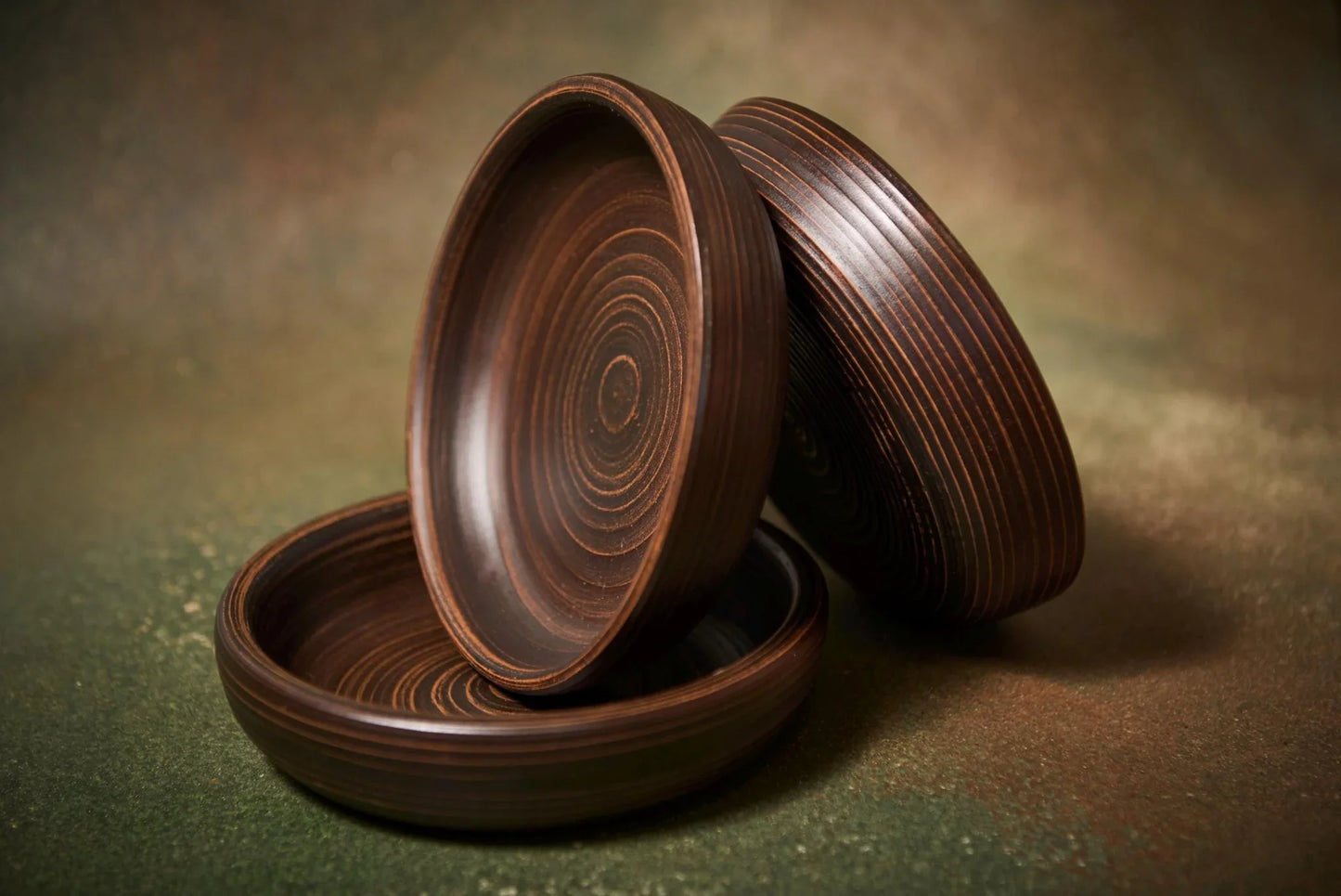 Three handmade brown clay bowls with concentric spiral textures on a dark rustic background