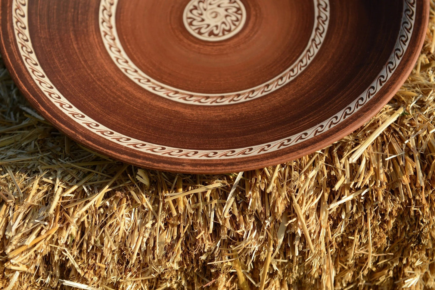 Handmade brown ceramic plate with decorative pattern on straw, artisan clay tableware