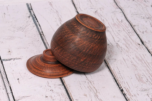 Handcrafted brown ceramic clay pot and lid on rustic white wood surface, artisanal cookware