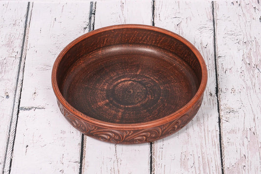 Handcrafted round ceramic baking dish with organic clay and decorative rim on rustic wood