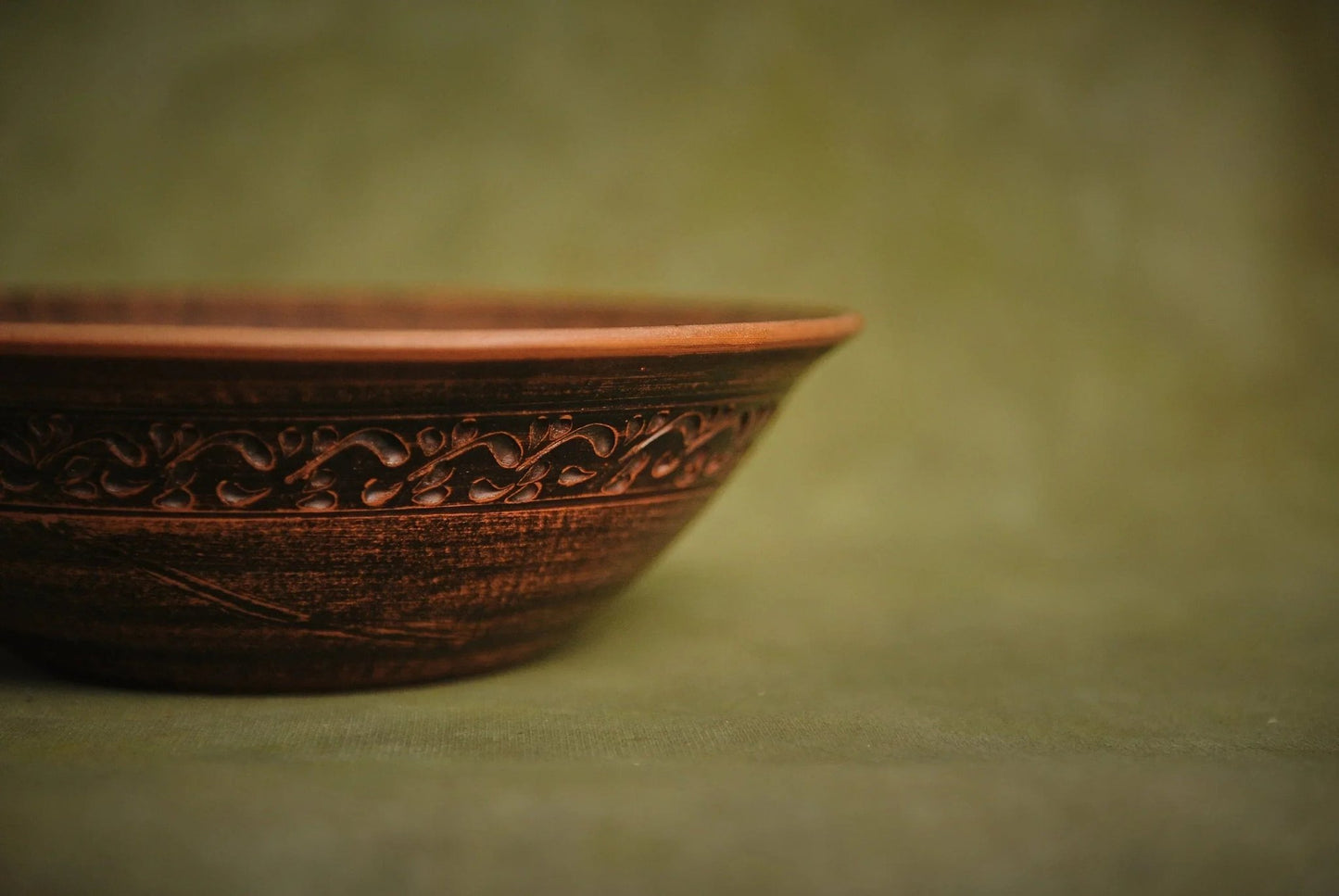Handmade brown ceramic bowl with ornate clay detailing on a green background