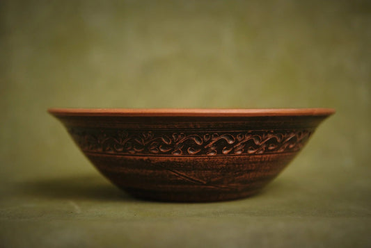Handmade red clay ceramic bowl with carved floral pattern on a neutral background