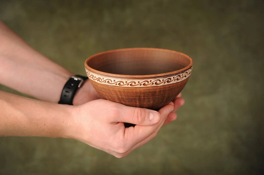 Hand holding a handmade rustic brown ceramic bowl with decorative clay rim, artisan pottery