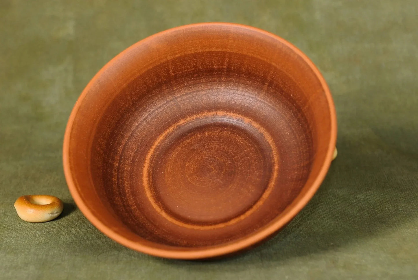 Handmade brown ceramic clay bowl on green fabric surface, artisan pottery homeware