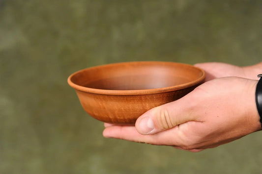 Hand holding a handmade brown clay ceramic bowl with matte finish, rustic homeware