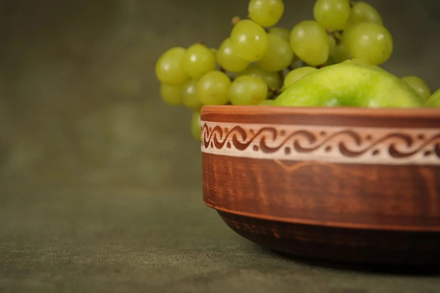 Handmade ceramic clay bowl with rustic pattern filled with green grapes and apple