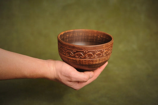 Hand holding a handmade deep red clay ceramic bowl with ornate carved pattern, artisan pottery