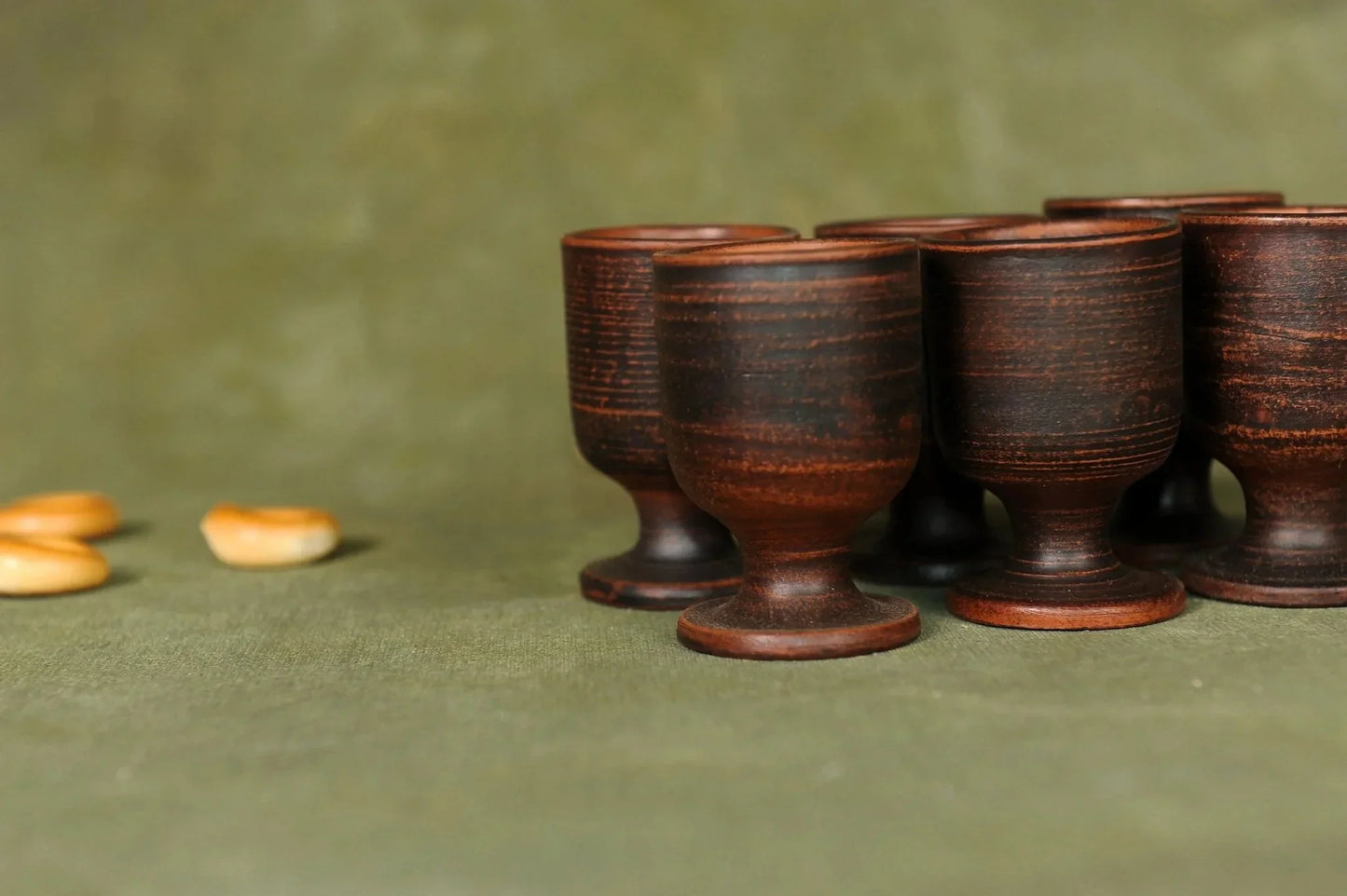 Handmade clay pottery shot glasses set of six on green background, artisan drinkware