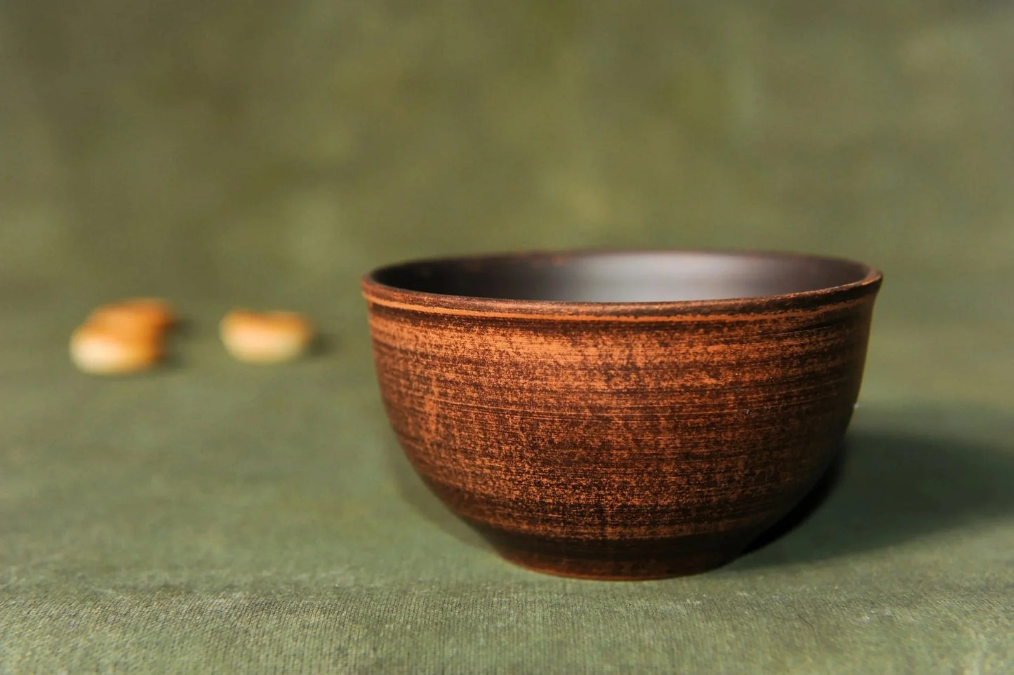 Handmade rustic ceramic dipping bowl, brown pottery cup on green background, clay homeware