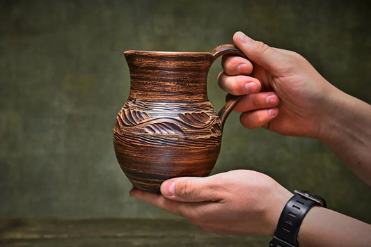 Hand holding a handmade ceramic clay jug with carved detailing, artisan pottery home decor.