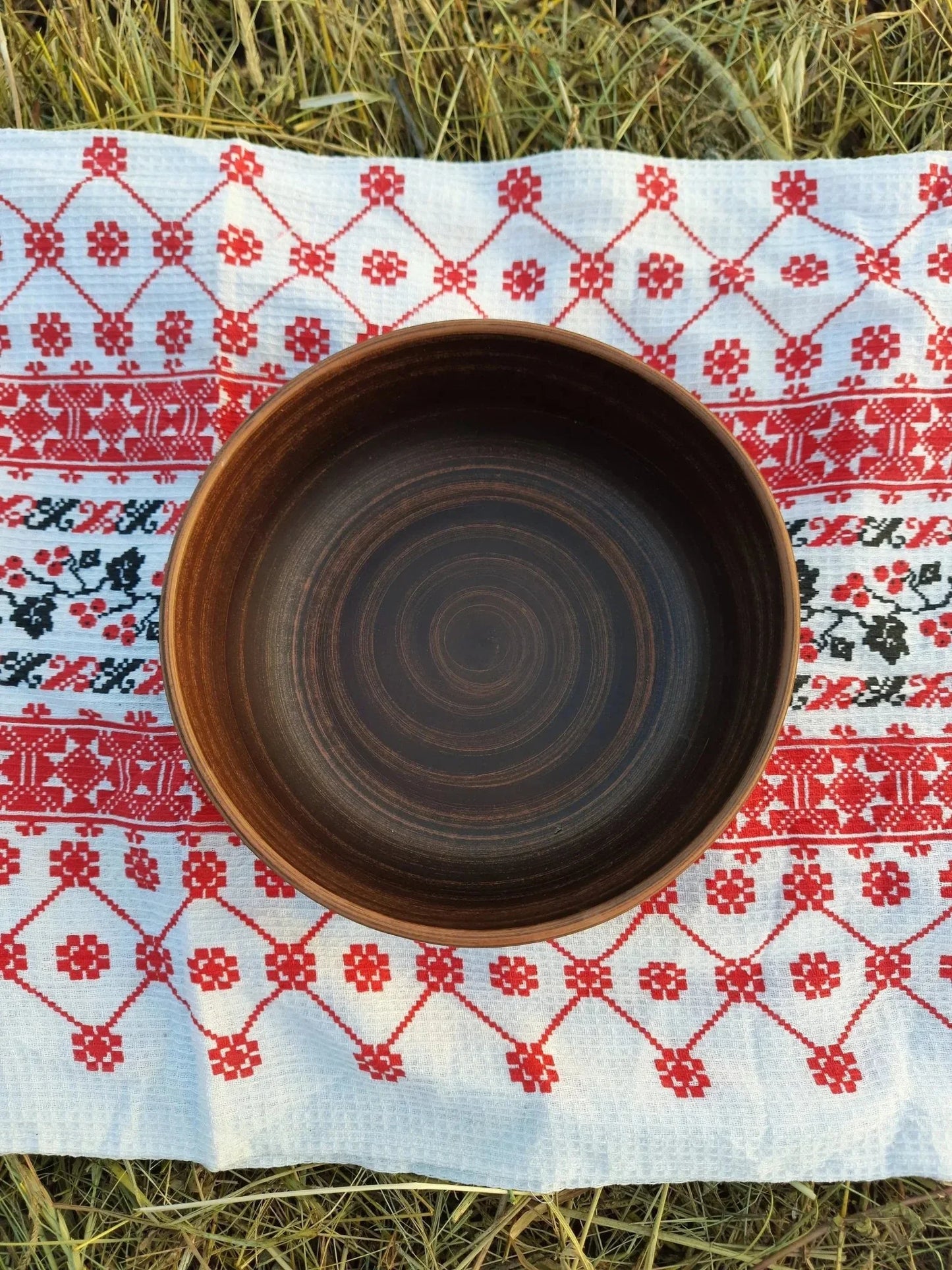 Handmade rustic clay bowl on embroidered cloth, artisan pottery homeware, outdoor setting