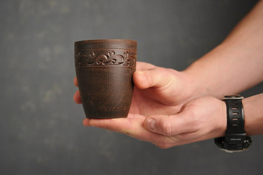 Hand holding a handmade engraved red clay drinking glass with floral detailing