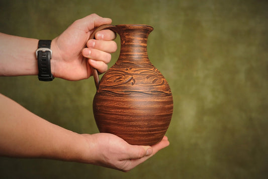 Hand holding a handcrafted ceramic clay jug with carved design, artisan homeware