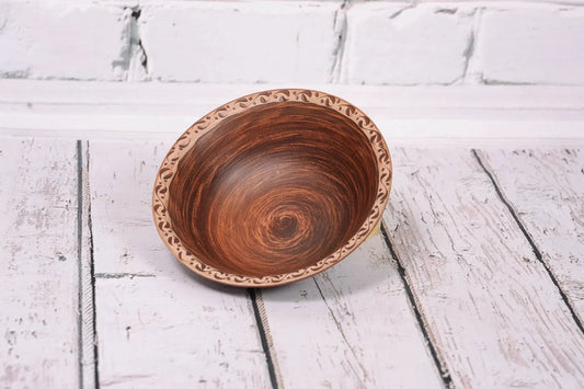 Handmade clay bowl with decorative rim, rustic pottery for soup, on white wooden background