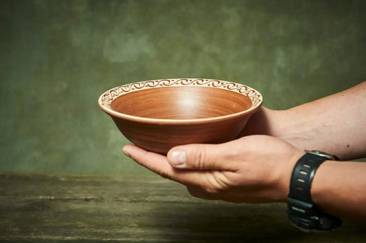 Hand holding a handmade clay bowl with rustic engraved rim, artisan ceramic dishware