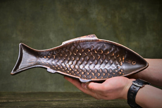 Handmade brown clay fish plate with textured scales, held in hands, artisan pottery homeware