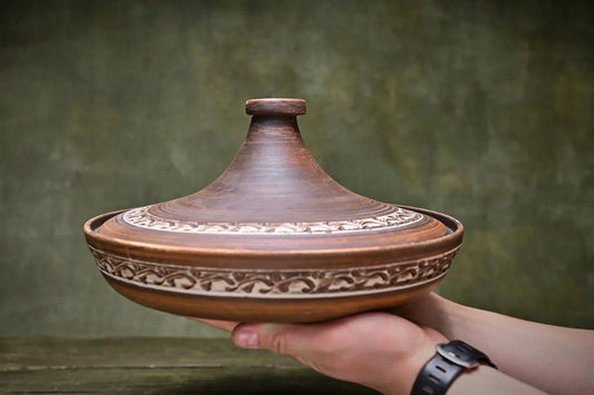 Handmade ceramic tagine pot with intricate pattern, held in hands, artisan clay cookware