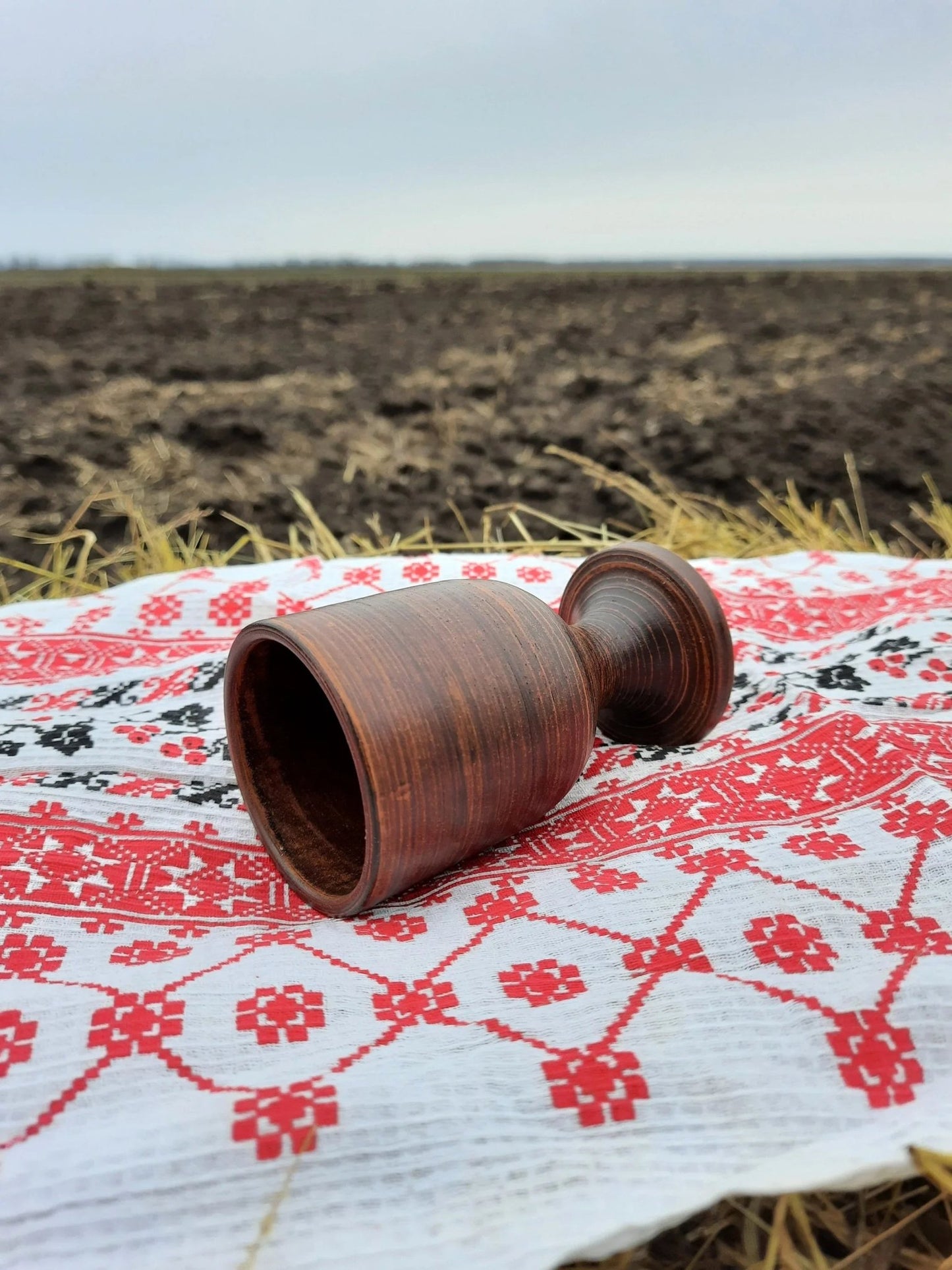 Handmade clay wine glass on embroidered cloth, outdoors on a field, artisan homeware.