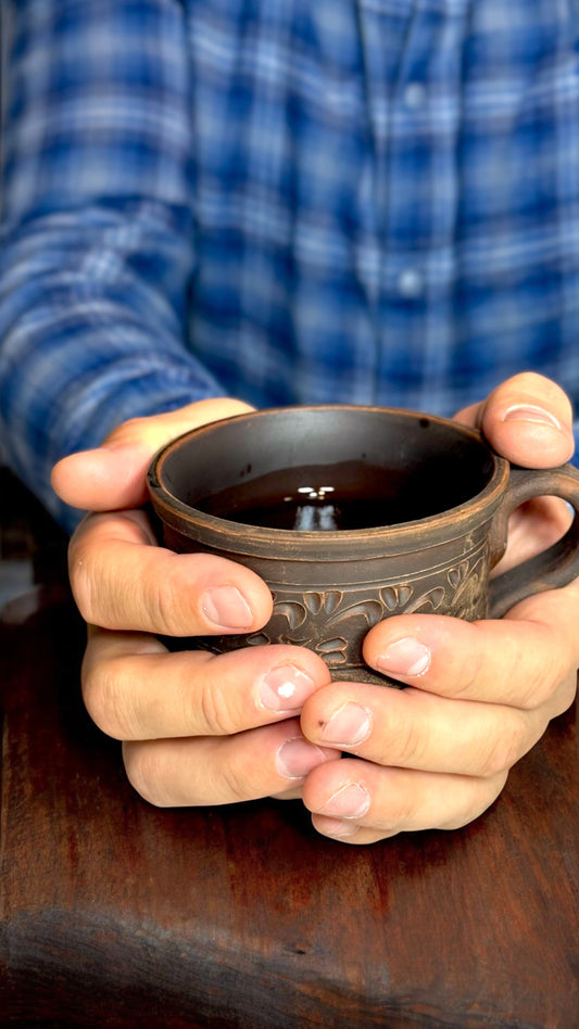 Handcrafted ceramic pitcher with engraved pattern on a rustic wooden surface, soft natural light