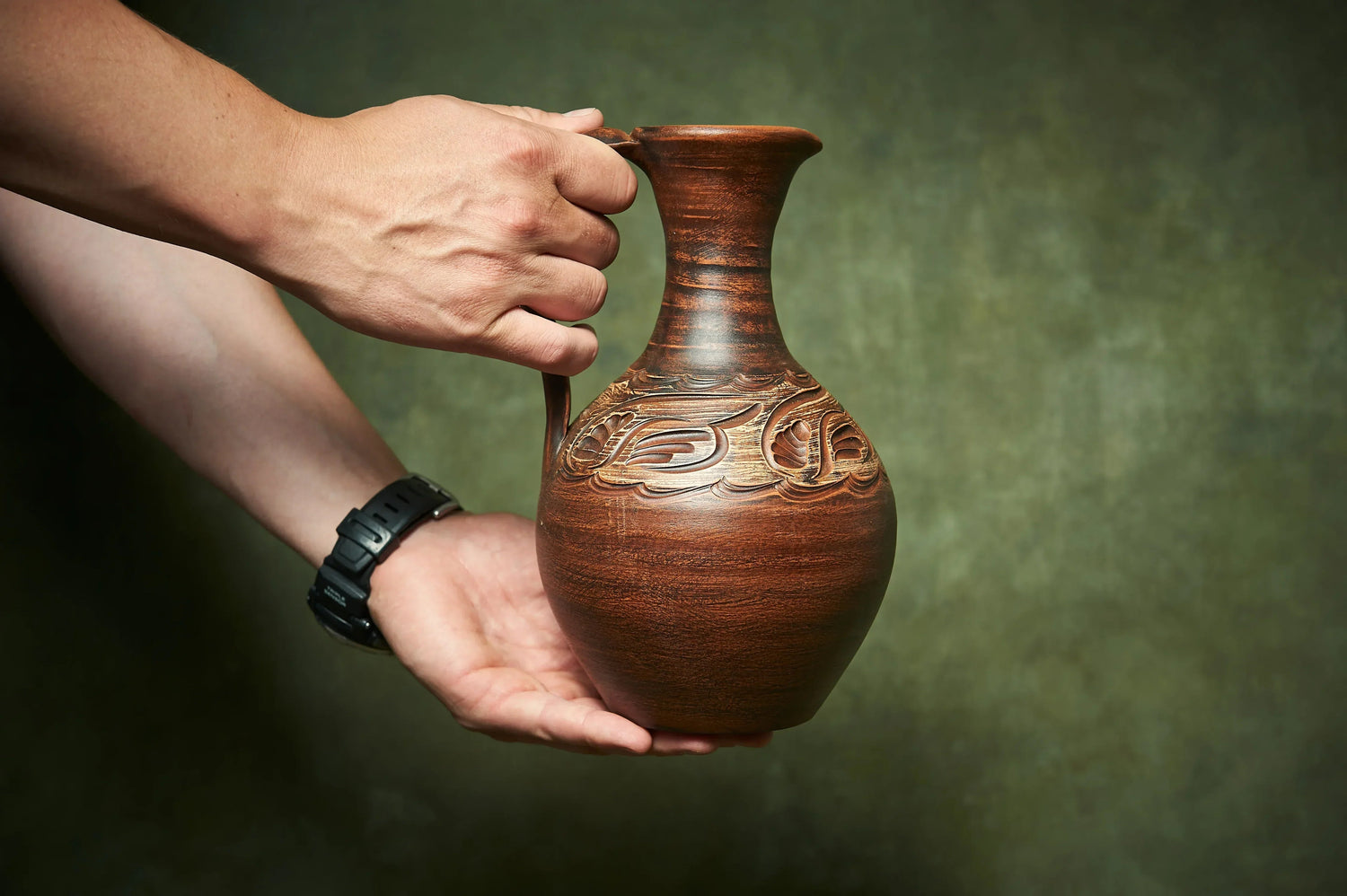 Hand holding handmade brown clay jug with carved details, artisan homeware décor
