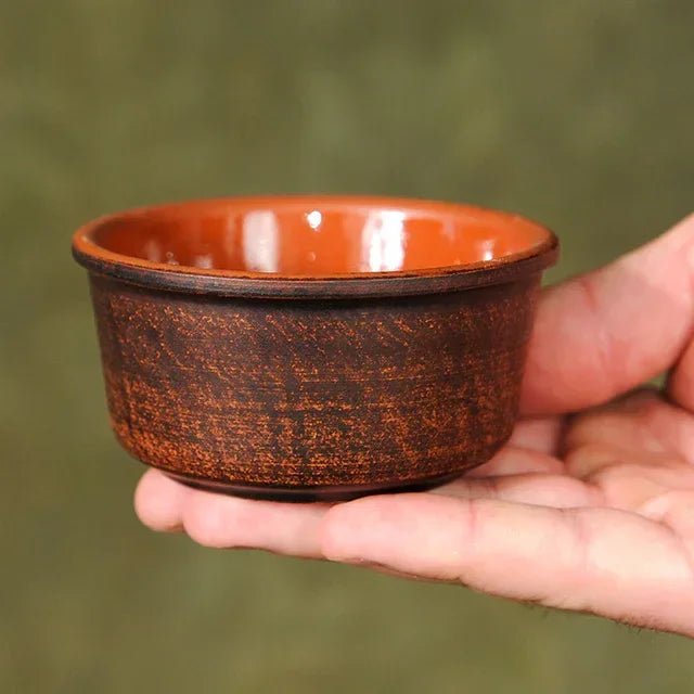 Hand holding a handcrafted ceramic bowl with brown textured exterior and glossy orange interior