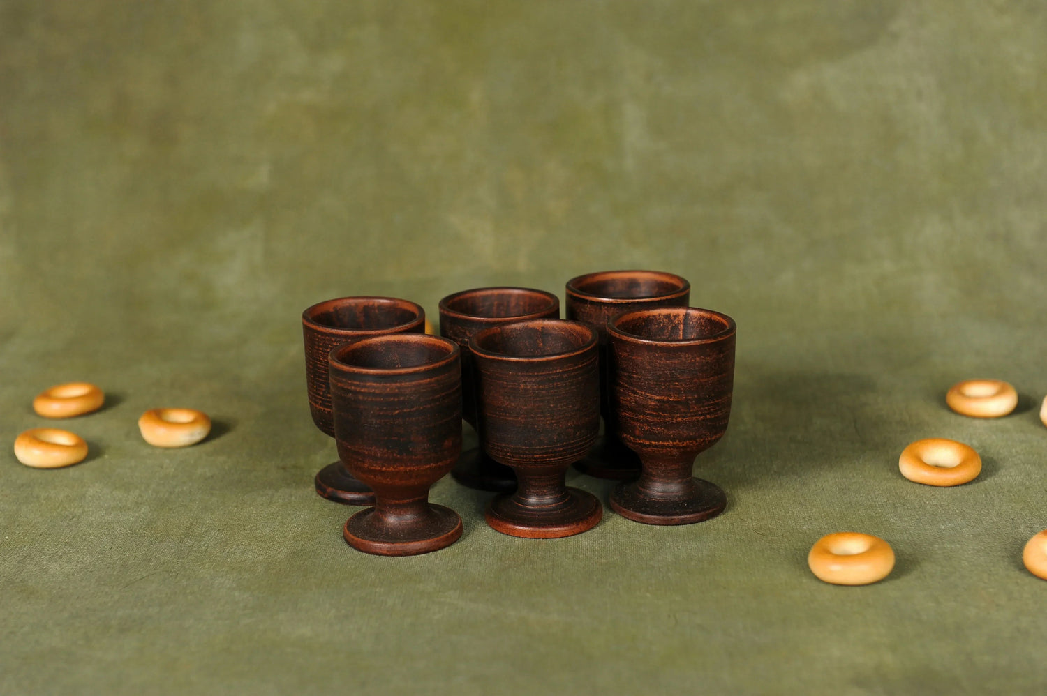 Set of six handcrafted clay ceramic cups with a rustic brown finish on a green background