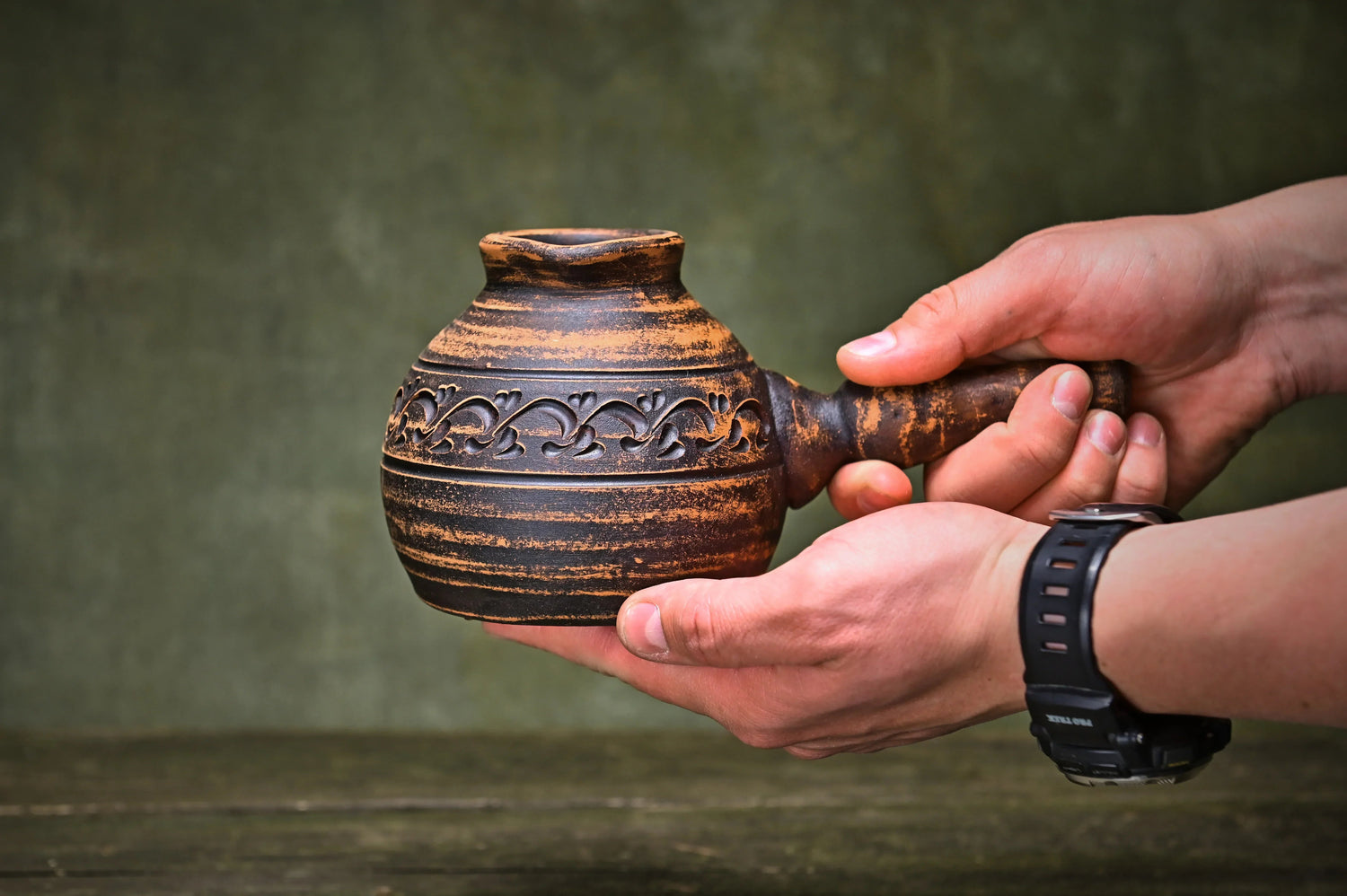Hand holding a rustic handmade clay teapot with carved floral details, artisan homeware