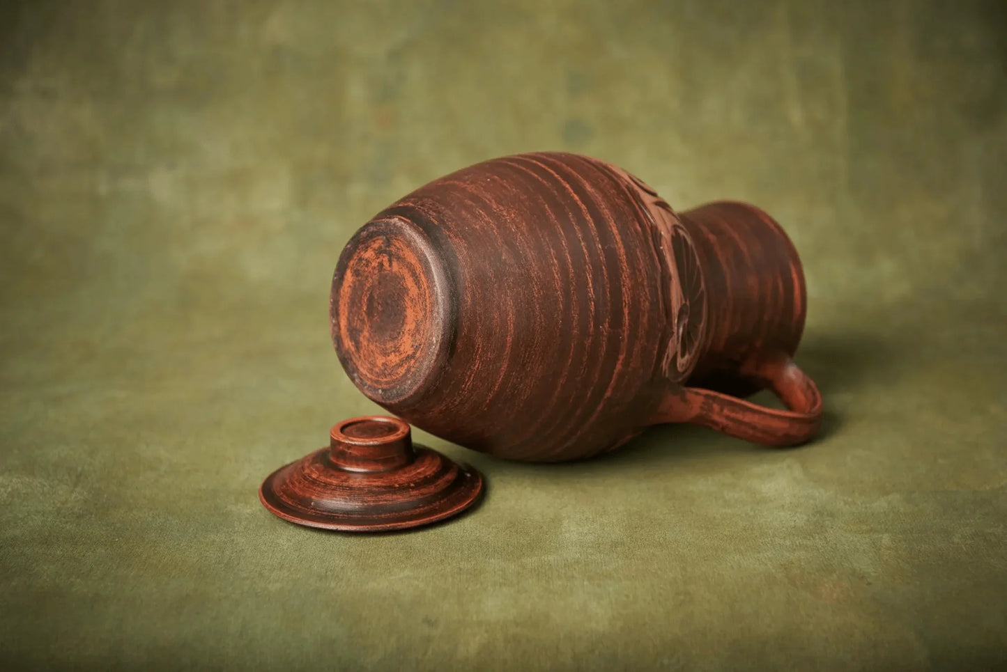 Handmade clay jug with lid, rustic ceramic homeware on green background