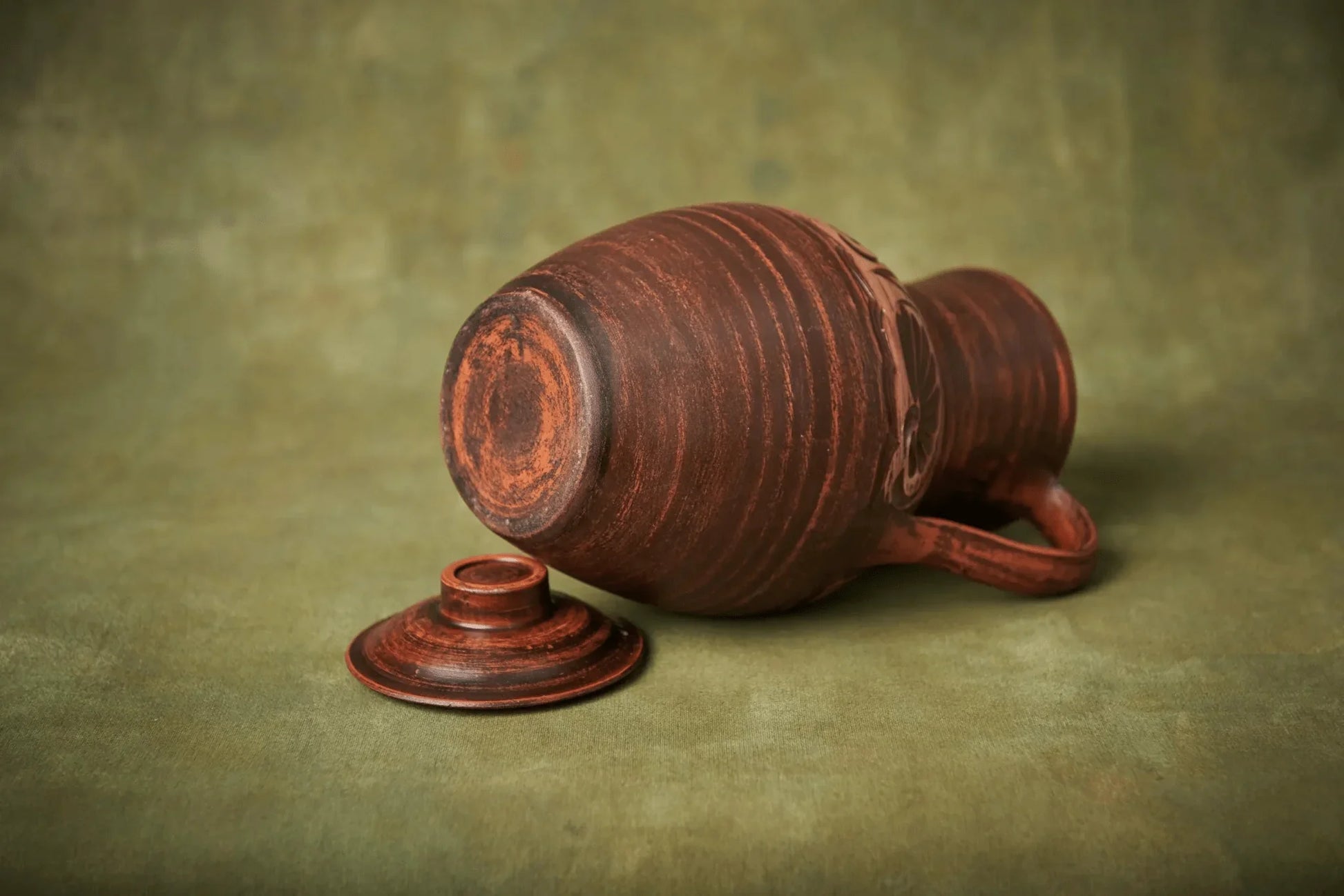 Handmade clay jug with lid, rustic ceramic homeware on green background