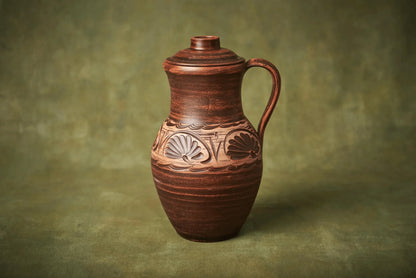 Handmade clay jug with lid and carved design, artisan ceramic homeware on green background