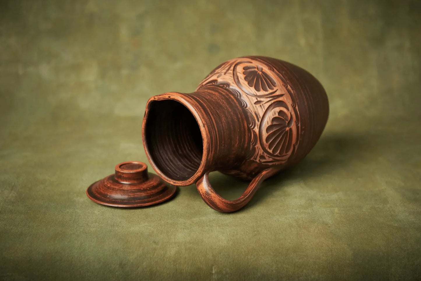 Handmade clay jug with lid, artisan ceramic vessel on green background from clayproductsshop