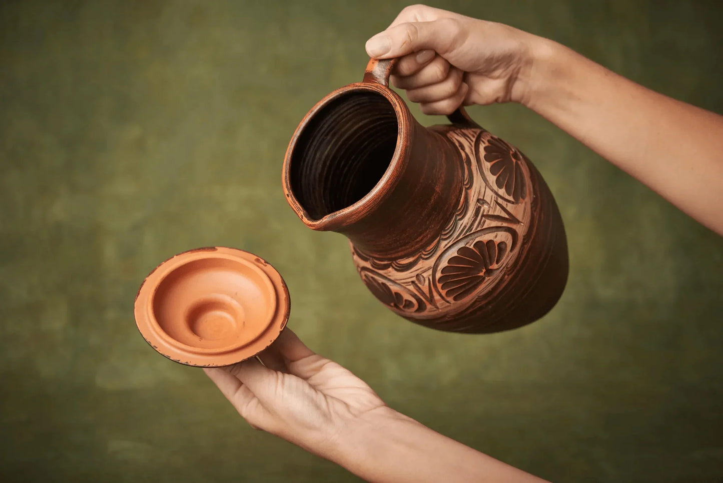 Hand holding a large handmade clay jug with lid, artisan ceramic vessel, rustic homeware